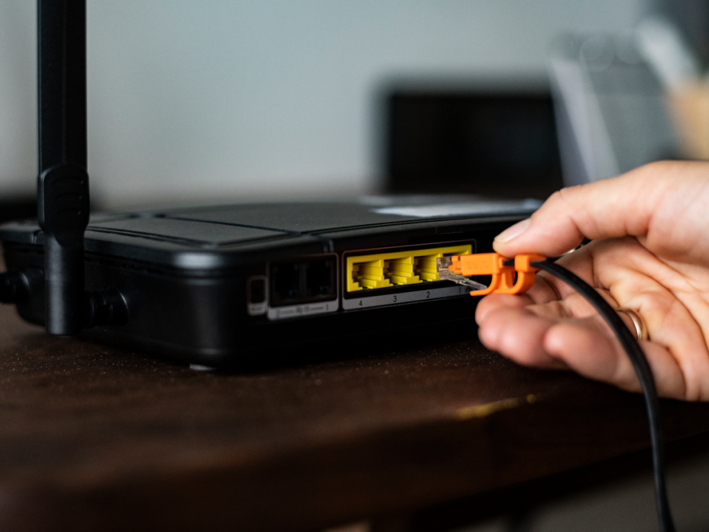 Mão segurando o cabo ethernet que se encaixa no roteador de internet, simbolizando a necessidade do acesso a internet para o uso do IPTV.