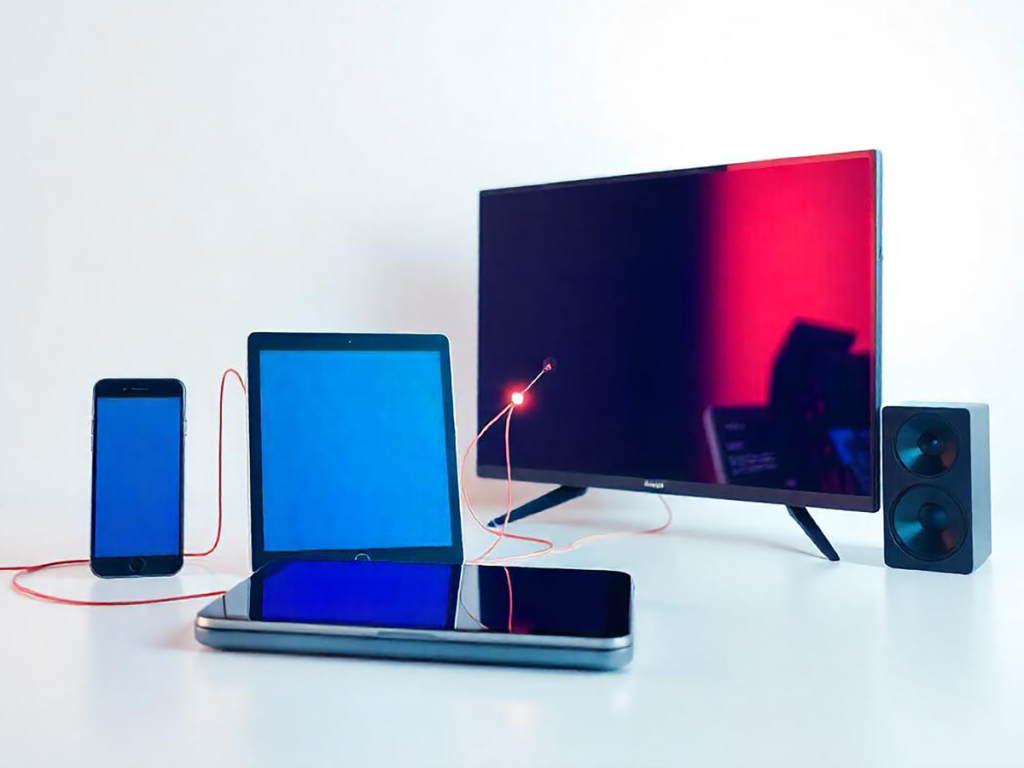 Diferentes dispositivos (smartphone, tablet, TV, etc) em uma mesa branca, representando a compatibilidade de listas m3u em diferentes sistemas.