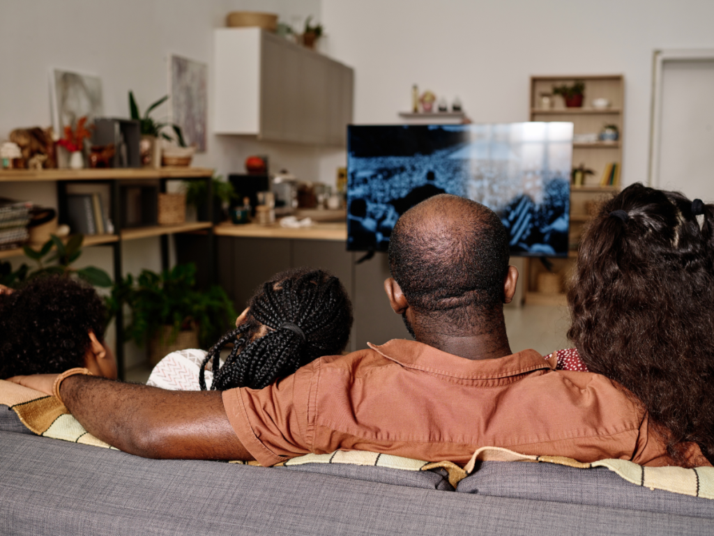 Família assistindo TV reunida no sofá de casa, representando a experiência de entretenimento compartilhado proporcionada por serviços durante o teste IPTV gratuito.