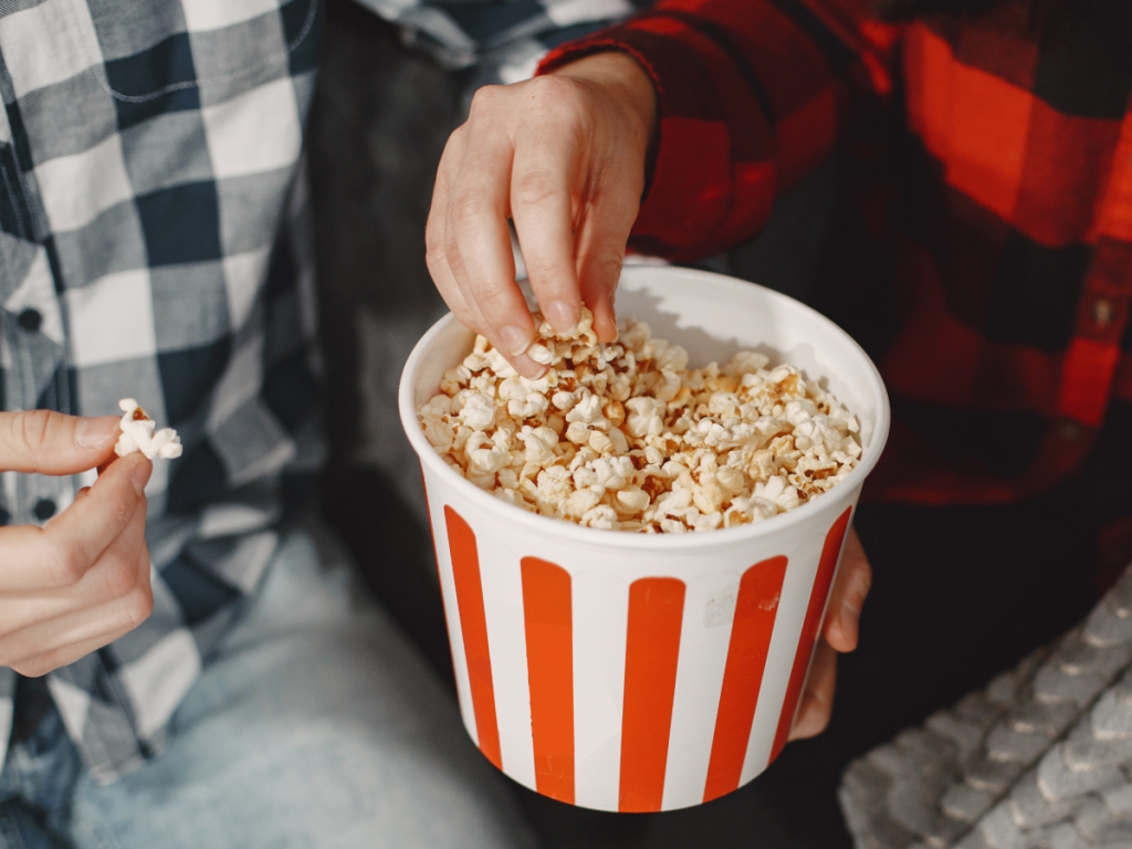 Balde de pipoca sendo compartilhado por duas pessoas enquanto assistem filmes de ação.