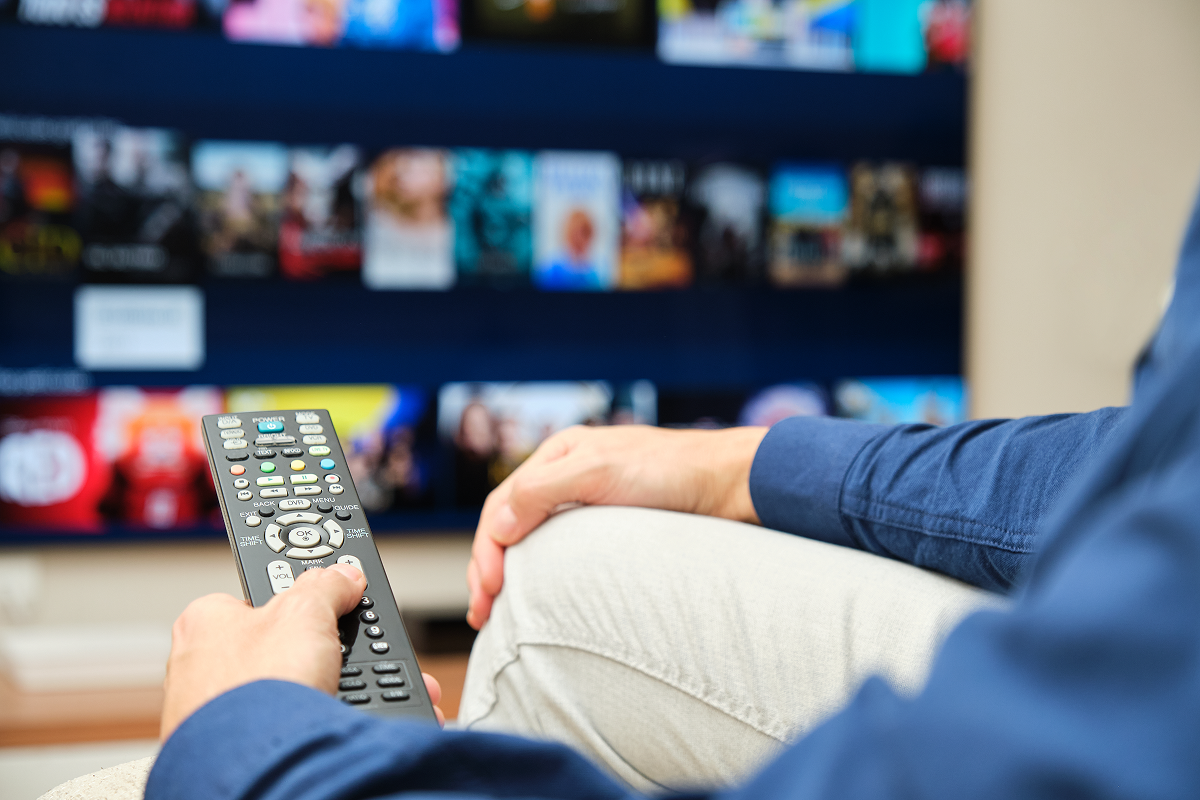 Imagem de uma pessoa segurando um controle, e á frente, uma TV, caracterizando o uso do IPTV Smarters Pro.