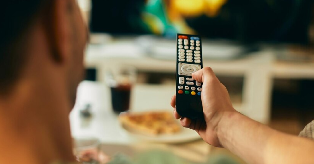 Homem em casa frustrado ao assistir TV devido a travamentos ou erro de transmissão, representando interrupções comuns em serviços de IPTV travando.