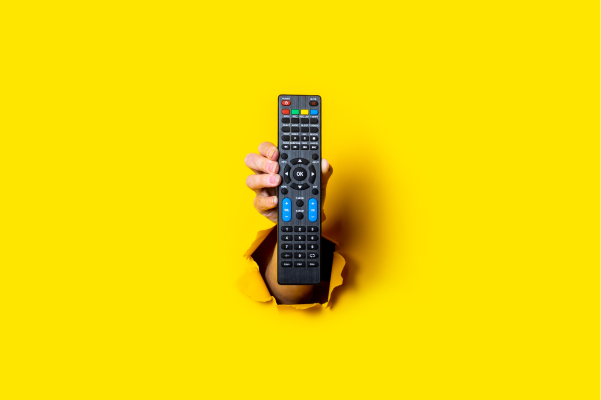 Controle remoto saindo de um fundo amarelo, simbolizando a liberdade e variedade de escolha ao acessar aplicativos IPTV para Smart TV.