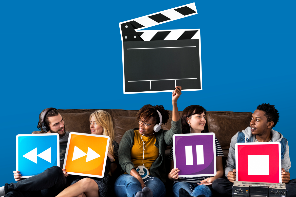 Grupo de amigos sentados no chão segurando ícones de controle de mídia, como retroceder, avançar, pausar e parar, enquanto uma pessoa segura um clapperboard de cinema. A imagem representa canais de filmes e séries, além de diversão, interação social e entretenimento audiovisual em um ambiente descontraído