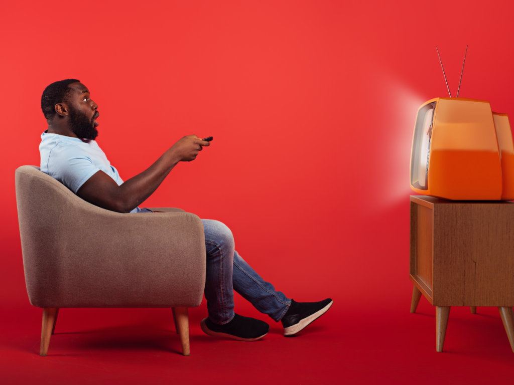Homem em poltrona assistindo uma TV antiga com expressão surpresa, destacando o contraste entre tecnologia moderna e limitações das listas IPTV gratuitas.