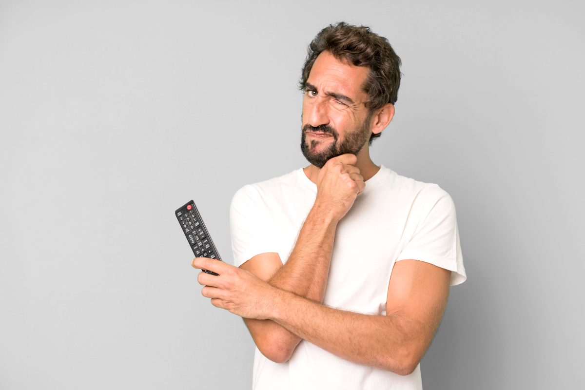Homem segurando um controle remoto com expressão de dúvida, representando questionamentos sobre o uso de lista grátis IPTV.