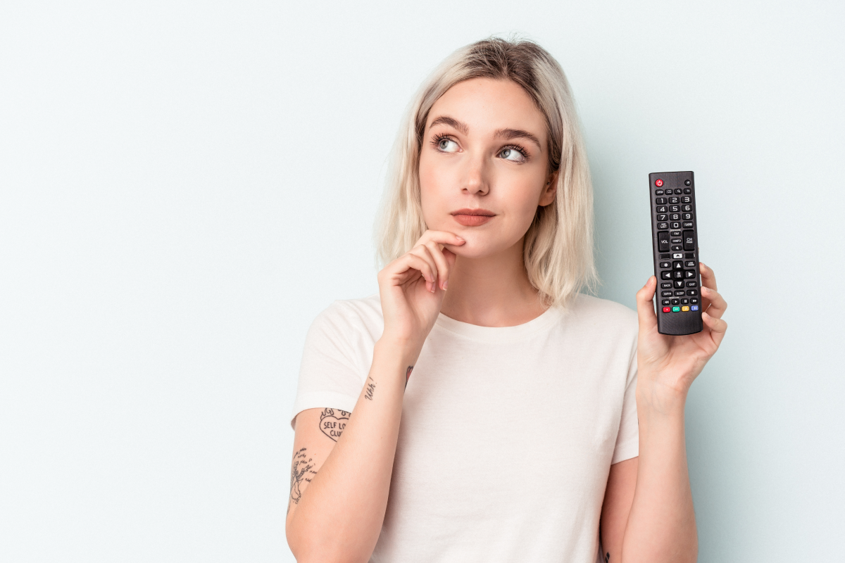 Mulher segurando controle remoto com expressão pensativa, representando a escolha do melhor IPTV gratuito para assistir TV online.