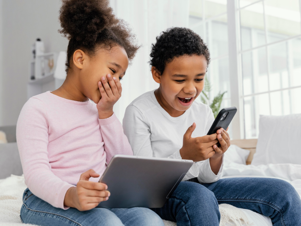 Duas crianças sorrindo enquanto usam um tablet e um smartphone para assistir canais infantis no IPTV.