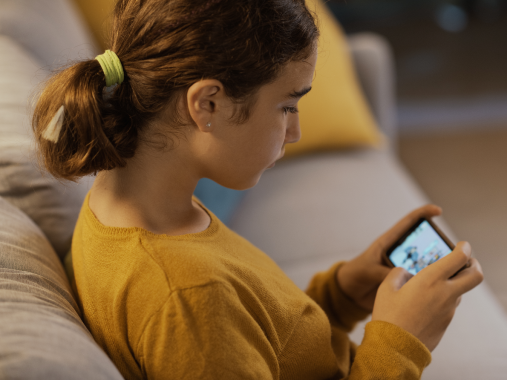 Menina concentrada assistindo a conteúdo em um smartphone, representando o fácil uso de aplicativo IPTV em dispositivos móveis.