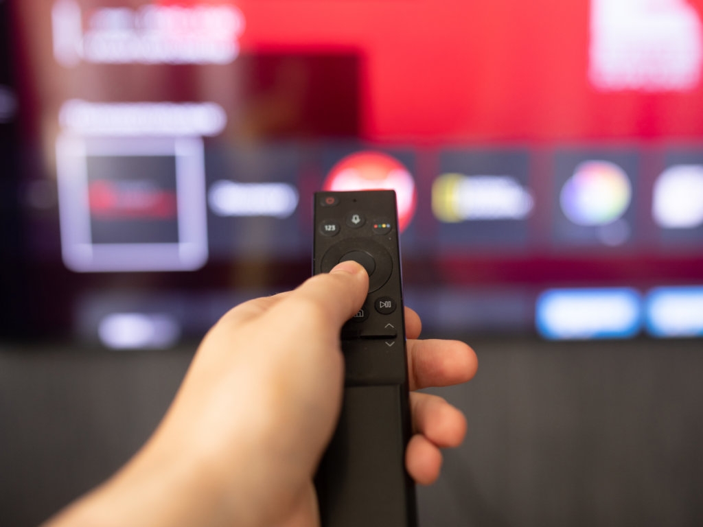 Mão segurando controle remoto inteligente apontado para uma smart TV com aplicativos em destaque, simbolizando o uso do Fire Stick com IPTV.