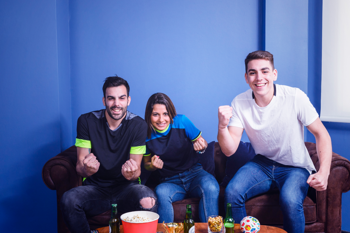 Amigos reunidos na sala de estar assistindo esportes ao vivo por IPTV, torcendo com pipoca e bebidas durante o jogo.