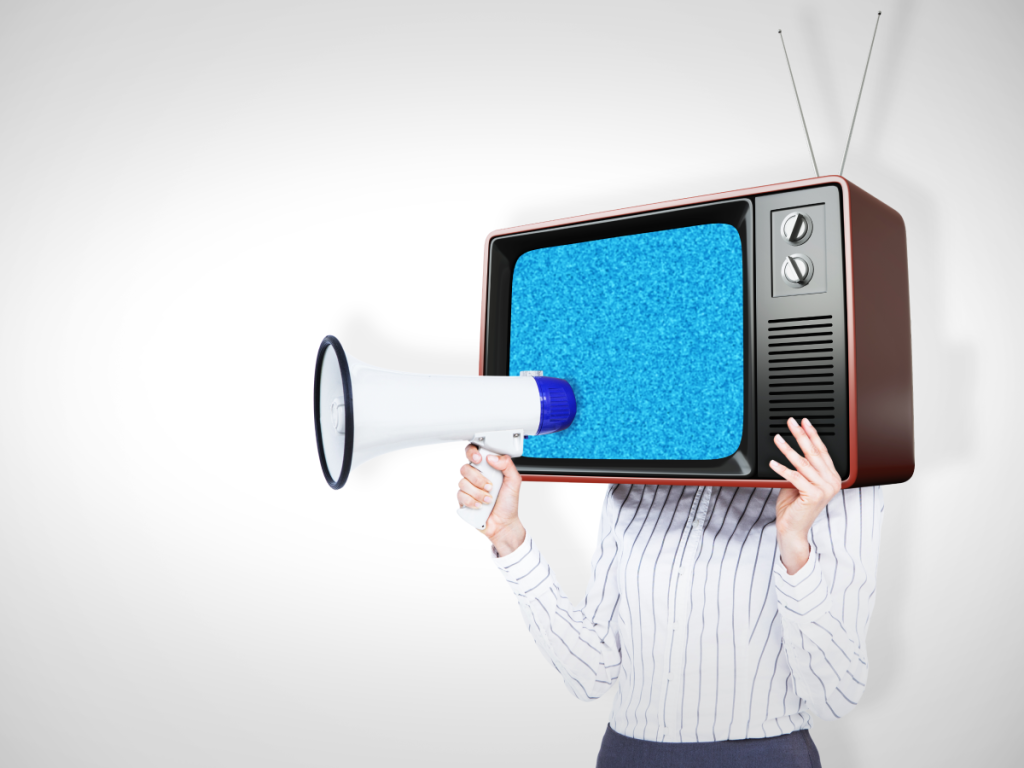 Pessoa usando uma televisão retrô como capacete e segurando um megafone, em alusão a séries de comédia criativas.