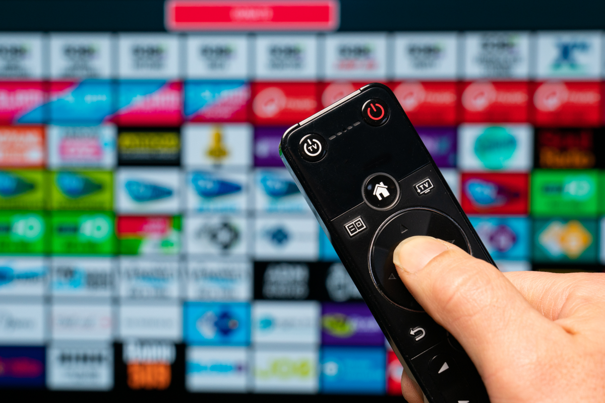 Imagem de uma tela com diversos aplicativos de lista IPTV grátis, com uma mão manuseando um controle de TV.
